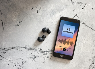 Smartphone with audiobook app and wireless earbuds on gray background