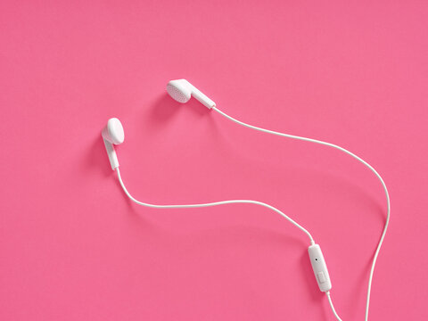White wired earbuds resting on pink background