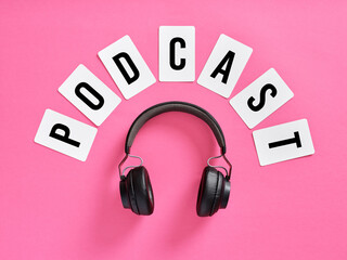Podcast word and headphones on pink background, symbolizing listening to podcast.