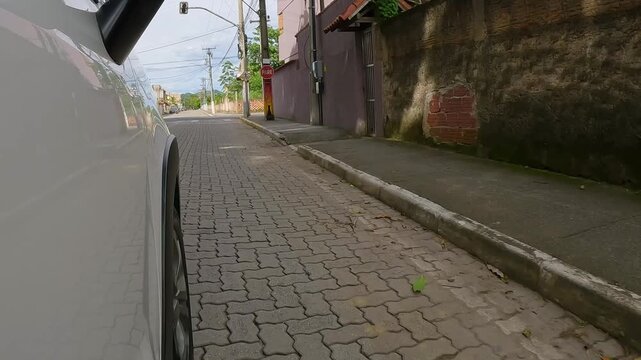 Side point of view shot of a white car driving over a speed bump on a paved suburban street with a wall and houses. Urban driving concept.