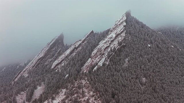 Snowing lightly still winter Flat Irons rock formations slabs Chautauqua Park Boulder Colorado USA aerial drone sunset dusk evening trees foggy low cloud layer snowing snow flakes snow falling circle