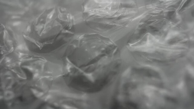 Close up abstract texture of transparent bubble wrap plastic. Soft focus, monochrome look, minimal packaging material background with subtle light reflections.