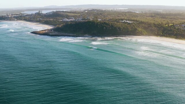 Aerial drone view of Falesias de Morro Branco showing curved coastline, sandy beach, rolling ocean waves, blue green water, and coastal landscape under daylight