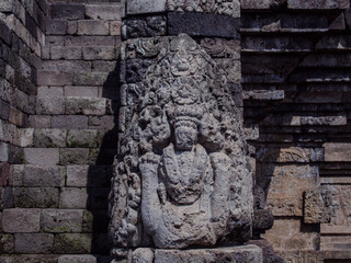 Ancient stone carving of a deity on a weathered brick wall, viewed from the front in bright sunlight.