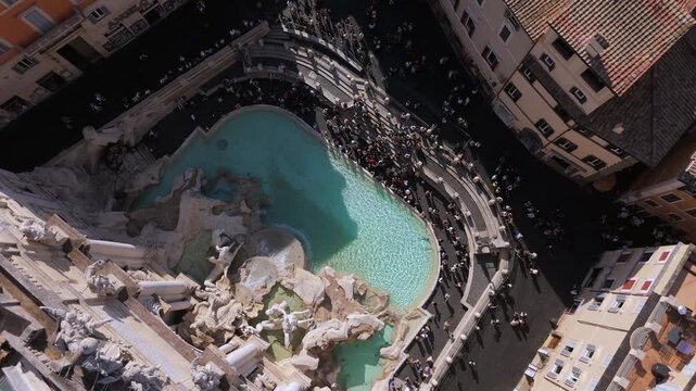 Aerial top down view of Trevi Fountain in Rome Italy showing iconic curved pool, ancient stone carvings, surrounding buildings and heavy tourist activity