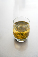 A glass of green tea with visible tea leaves inside