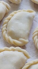 ​Close-up of raw homemade dumplings with beautiful braided edges on a floured wooden board.