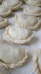 ​Close-up of raw homemade dumplings with beautiful braided edges on a floured wooden board.