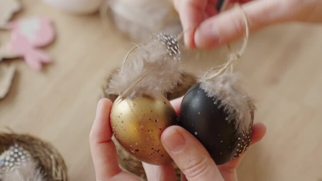 Close up of hands holding handmade Easter eggs decorated with feathers. Concept of DIY holiday decor and spring craft preparation.