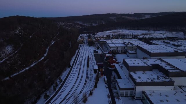 Aerial view of snow-covered transport and industrial area in Warstein, Germany, with train tracks, containers and brewery buildings at dusk under cold winter sky. Warsteiner Beer.