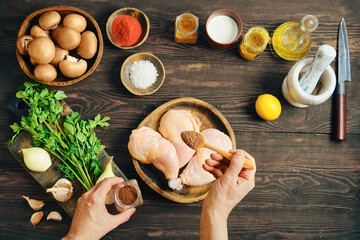 Hands seasoning raw chicken legs with spice on rustic wooden table with ingredients