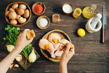Hands seasoning raw chicken legs with curry on wooden tabletop with ingredients