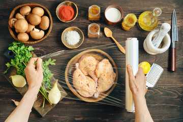 Hands wrapping marinated chicken with plastic stretch film for marinating or storage