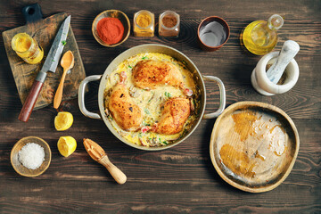 Cooking chicken in a pot with spices and fresh ingredients on a wooden table