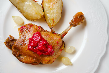Duck confit served with roasted potatoes and sauce on a white plate