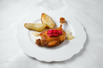 Duck confit served on a plate with potato wedges and red sauce at a dining table