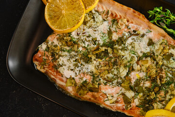Cooking pink salmon with herbs and lemon on a black plate in a kitchen setting