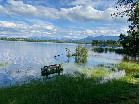 Wooden bench surrounded by water at Lake Staffelsee in Uffing am Staffelsee, Bavaria, Germany, after heavy rain and flooding. Green plants and vegetation are partially submerged in the lake. 