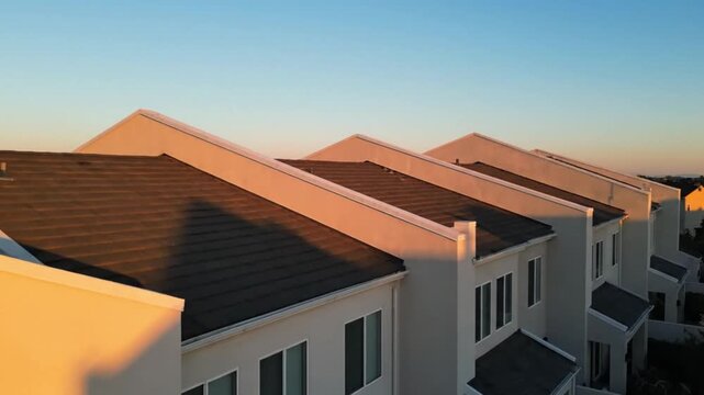 Aerial view of residential townhouses at sunset with golden light on roofs and clear blue sky.