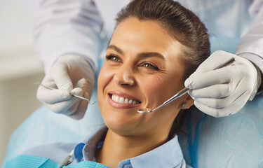 Happy woman smiling during routine checkup in dental clinic, dentists with tools checking teeth....