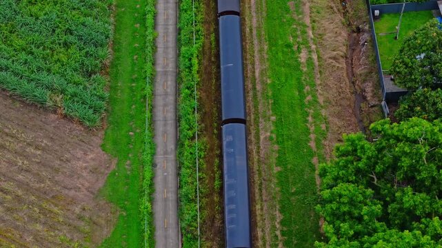 Top down aerial of Kuranda Scenic Railway tracks cutting through bright green tropical fields near Cairns