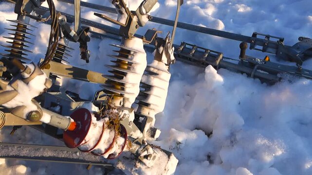 Detailed view of abandoned high voltage railway catenary insulators resting in deep snow, illuminated by warm sunlight with crisp shadows and visible ice textures.