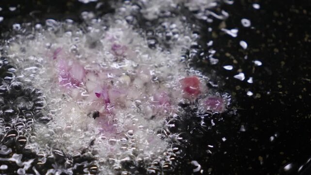 Close-up of red onion frying and sizzling in a hot pan with oil, turning glossy and soft for a recipe base, perfect for cooking, meal prep, and food content