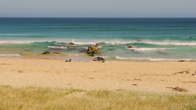 Slow motion landscape of ocean waves crashing on rocky boulders and seaside sandbar with beach towels and items laid on sand at beach in Yagon Seal Rocks in NSW Australia nature travel and outdoors