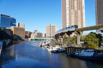 晴れた日の川沿いを走るモノレールと水面に浮かぶたくさんのボート