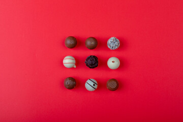 Overhead view of different chocolate spheres arranged on red background with copy space