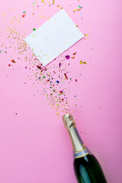 Overhead view of champagne bottle with scattered confetti with copy space on blank paper