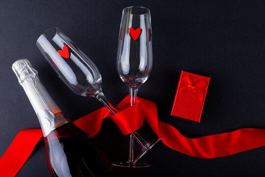 Champagne flutes tied with red ribbon by gift box and bottle on gray background, copy space