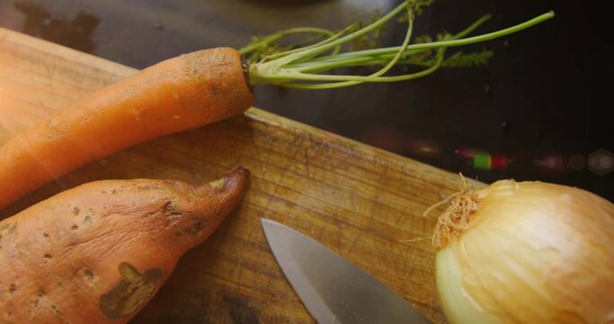Preparing dirt-speckled carrot, sweet potato, yellow onion on wooden board, chef knife and droplets