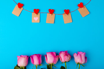 Overhead view of fresh pink roses and heart shaped decoration on blue background, copy space