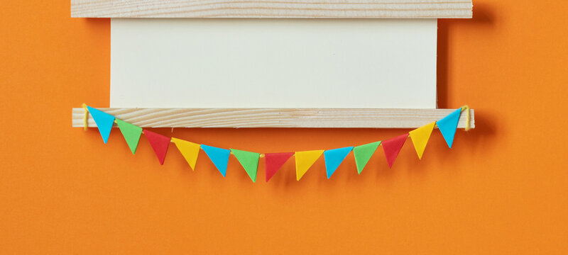 Festive invitation greeting card for birthday anniversary party carnival. Start of a project, business launch, opening ceremony. Wooden sign decorated with garland of flags. orange background