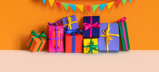 Fototapeta premium Festive holiday birthday poster with garland of flags, colorful gift boxes different size. orange wall background.