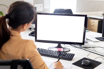 Rear view of businesswoman working on computer monitor at desk in office, copy space