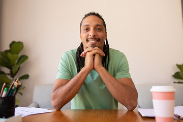 Portrait of smiling young businessman sitting with hands clasped at desk in workplace