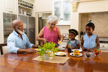 African american grandmother serving breakfast for her two granddaughters in kitchen at home