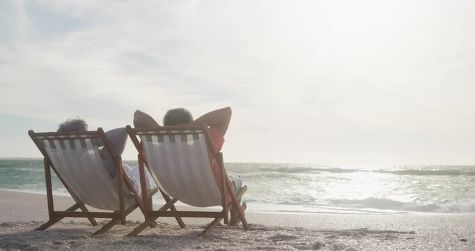Back view of senior couple relaxing on deckchairs on beach at sunset