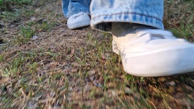 Women's feet in white sneakers walk in front of the camera. A walk in the forest. A woman in jeans and a light shirt is walking in the park or along forest paths. Active repair in the fresh air