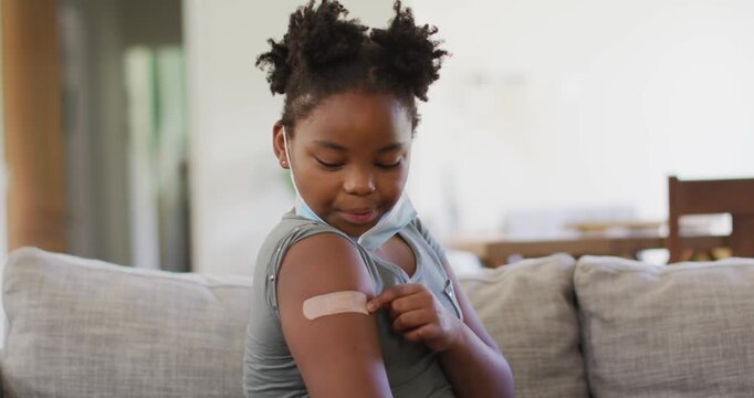 African american girl wearing face mask pointing at bandage on her arm