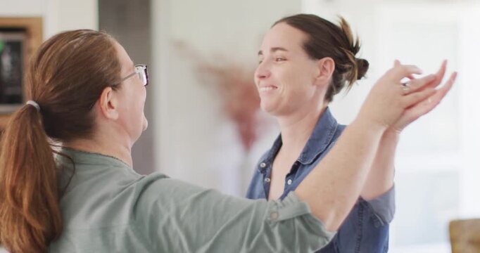 Caucasian lesbian couple smiling and dancing in kitchen
