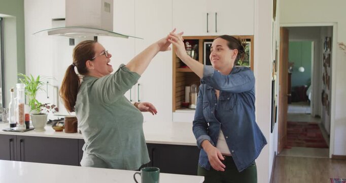 Caucasian lesbian couple smiling and dancing in kitchen