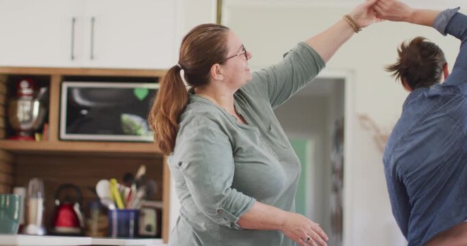 Caucasian lesbian couple smiling and dancing in kitchen