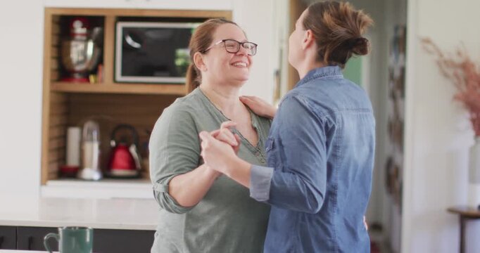 Caucasian lesbian couple smiling and dancing in kitchen