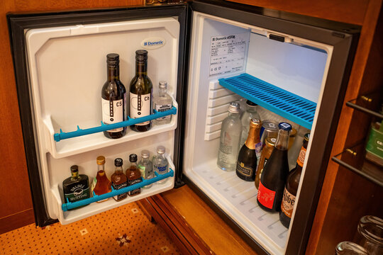 Open hotel room minibar fridge stocked with various alcohol bottles