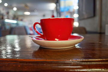 Fototapeta premium Red ceramic coffee cup on wooden table in cafe.