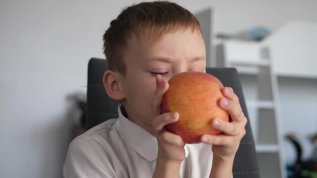 Cute boy eating a fresh red apple at home. Healthy snack and natural nutrition concept. 