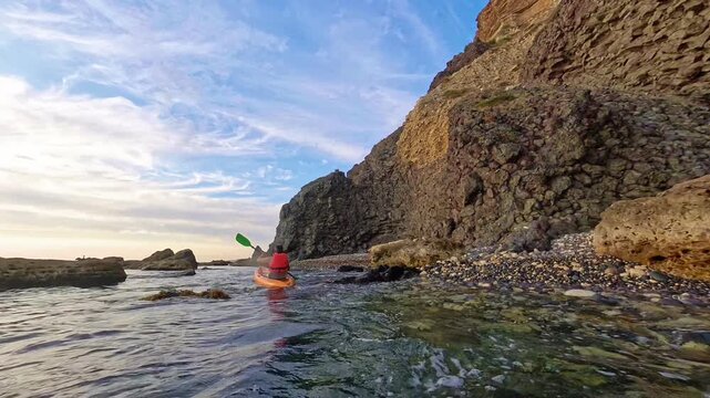 Kayak paddling sea man exploring rocky coastline in orange boat during a beautiful sunny summer day